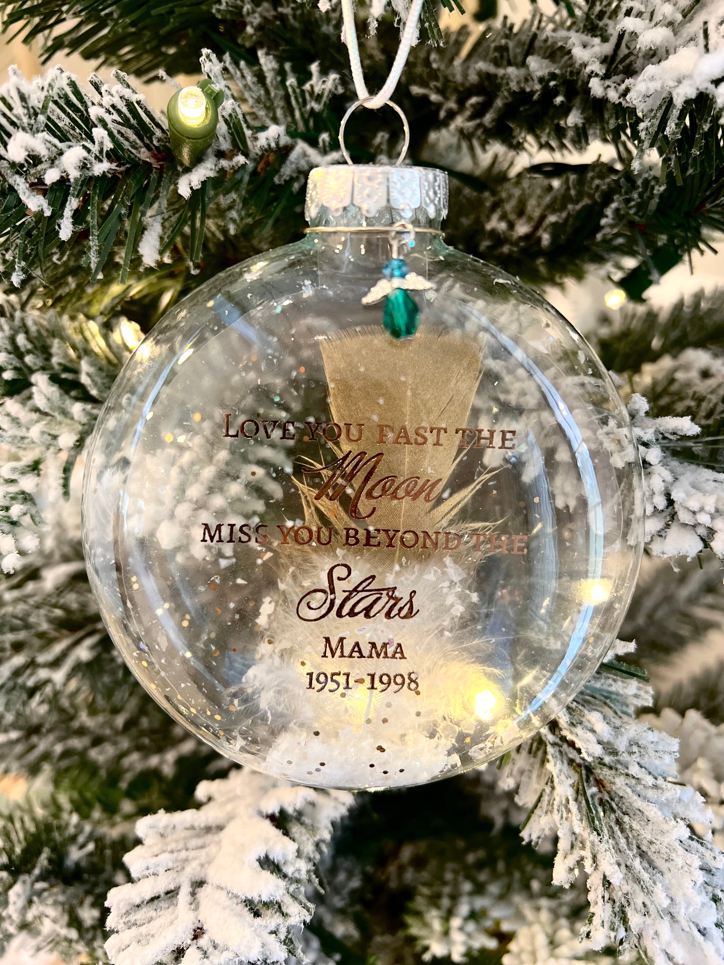 Close-up of the crystal angel charm and faux snow inside memorial ornament on a lighted Christmas tree branch laden with "snow"