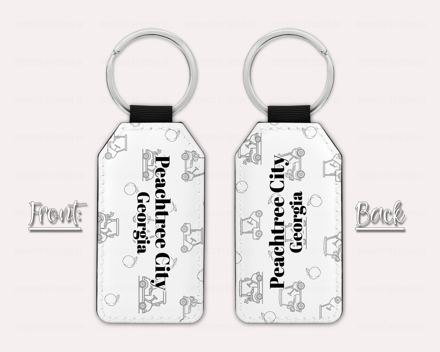 Exclusive design on 2 white faux leather keychain, with a golf cart and peach pattern text reads 'Peachtree City' with 'Georgia' placed right beneath. View of both sides on a pale pink background. Additional text on graphic reads "front' 'back' | imperfect by design co