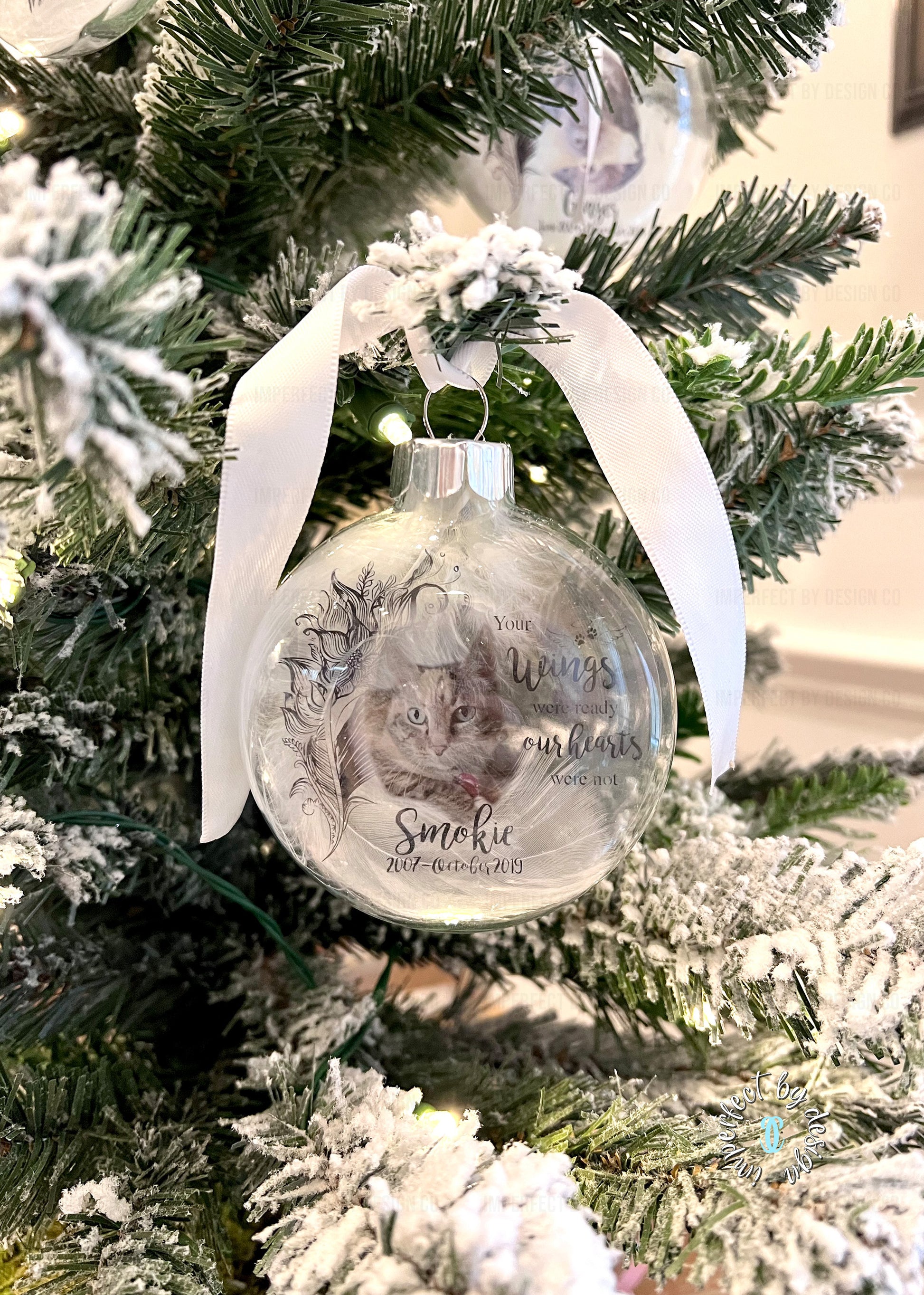 Close-up of glass memorial ornament with silver ribbon, personalized with pet's name, years of life, and memorial quote.