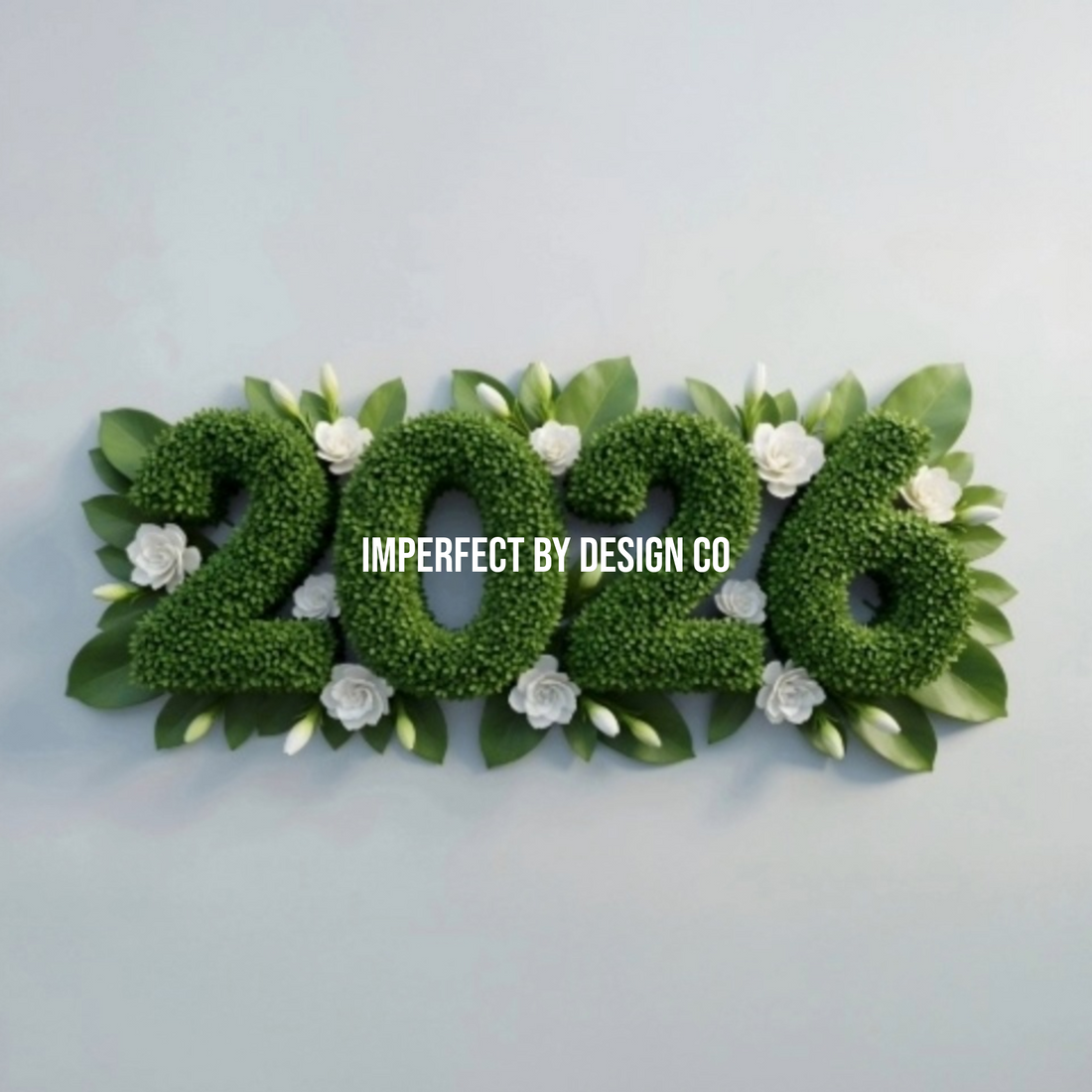 The numbers 2026 written as boxwood hedge flanked by small whit eflowers and green petals. imperfect by design co is written on top in white all cap letters.