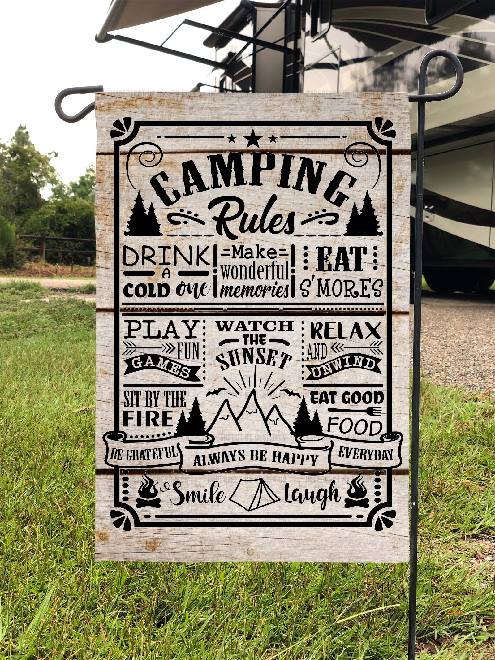 Camping-themed garden flag with 'Camping Rules" printed on it placed on garden flag stand in a campsite in front of a RV