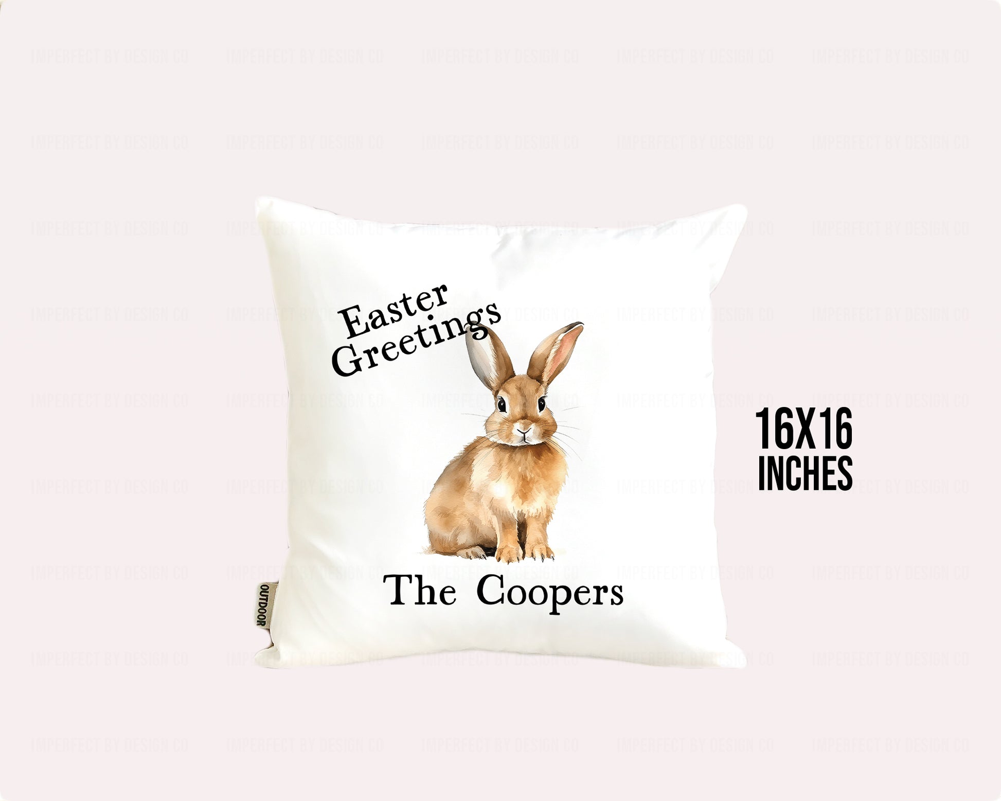 Decorative white indoor outdoor pillow advertising pillow cover featuring text that reads 'Easter Greetings - The Coopers' on pale pink background additional information on background states 16x16 inches
