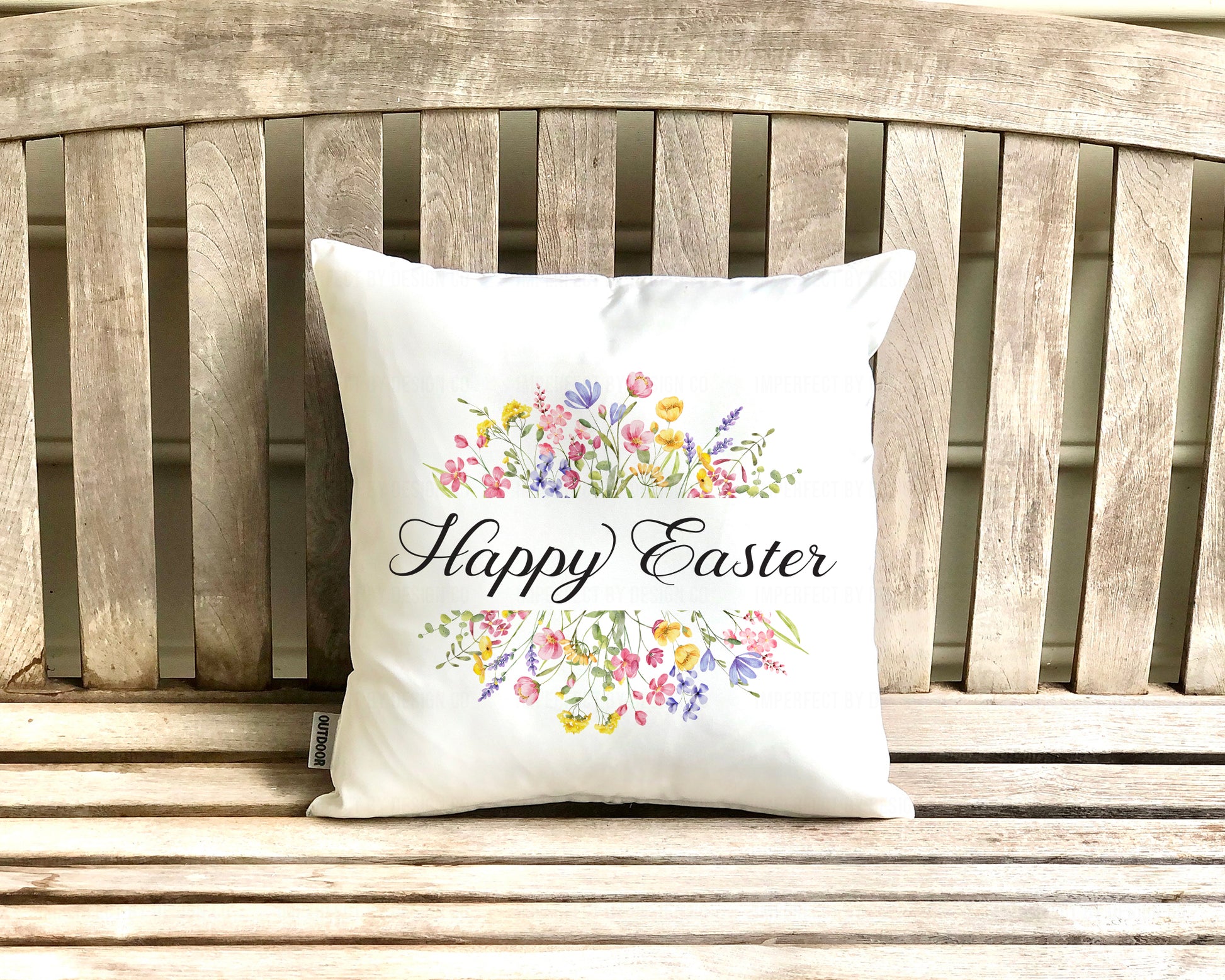 White pillow cover with 'Happy Easter' and floral designs on a wooden bench. imperfect by design co 