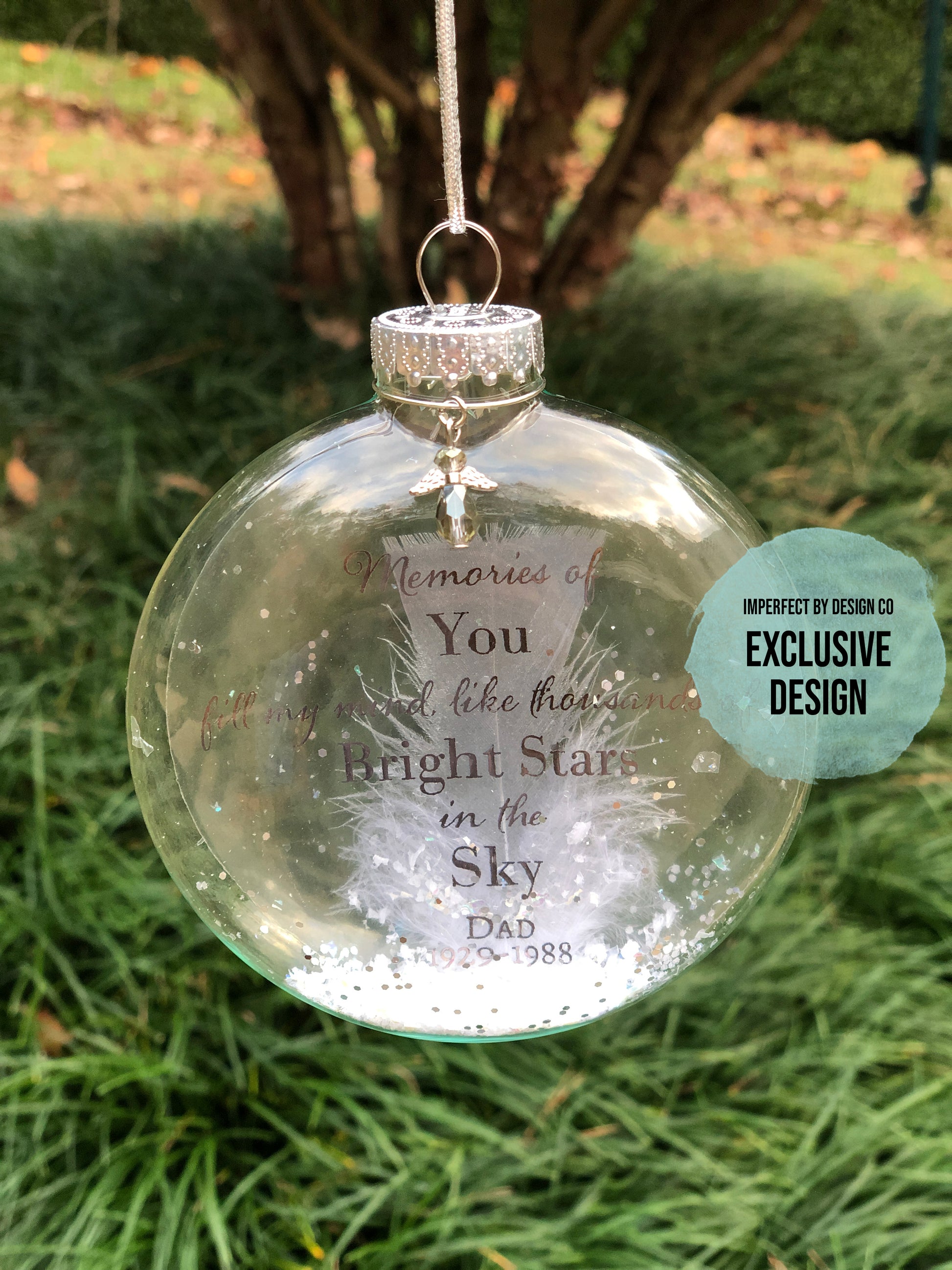 Close-up of personalized memorial ornament with pewter text and feather inside.