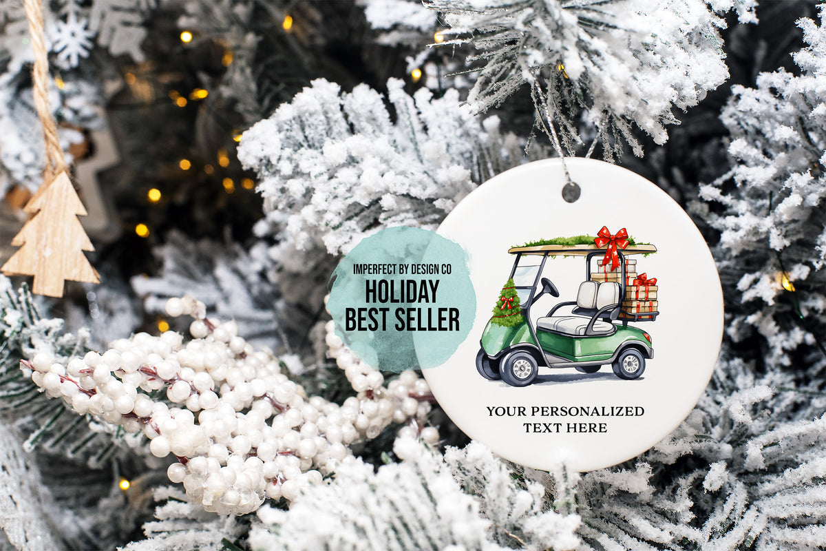 imperfect by design co exclusive design
A round white Christmas ornament hanging on a frosted Christmas tree. The ornament features an illustration of a green golf cart carrying a gift box with a red bow, plus printed text reading 'IMPERFECT BY DESIGN CO HOLIDAY BEST SELLER' and 'YOUR PERSONALIZED TEXT HERE'.