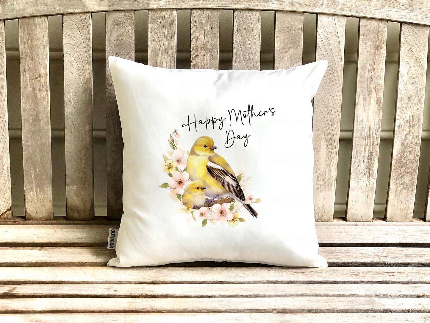 White decorative pillow cover (on a pillow pillow) with a female Goldfinch and it's nestling sitting on a branch with pink flowers. Text on pillow reads "Happy Mother's Day'. Placed on teak bench  | imperfect by design co