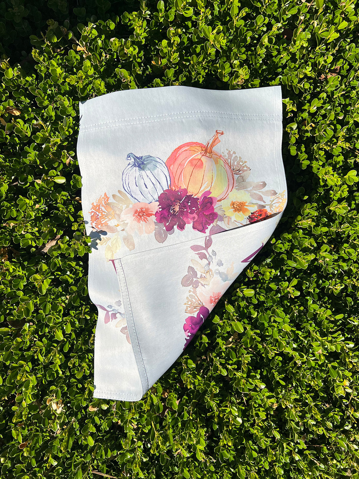 Exclusive design by imperfect by design co Garden Flag folded to show double sided print. Colorful print of pumpkins and flowers, laid flat on green grass. 