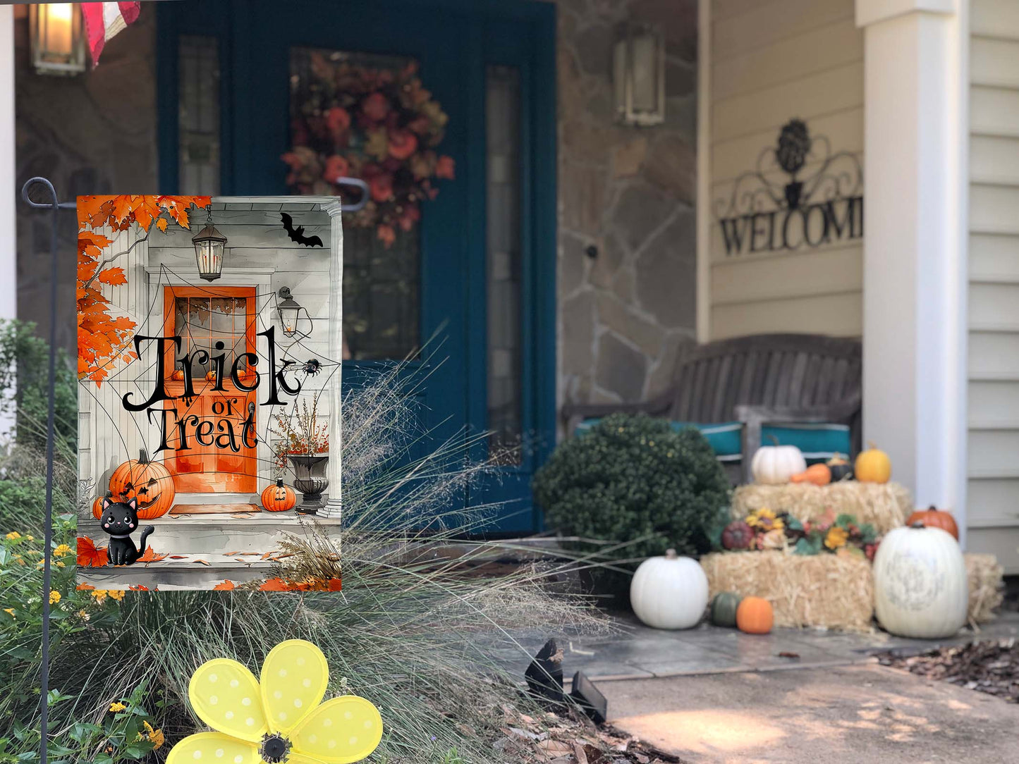 Cute black cat sitting in front of a decorated Halloween porch garden flag.
