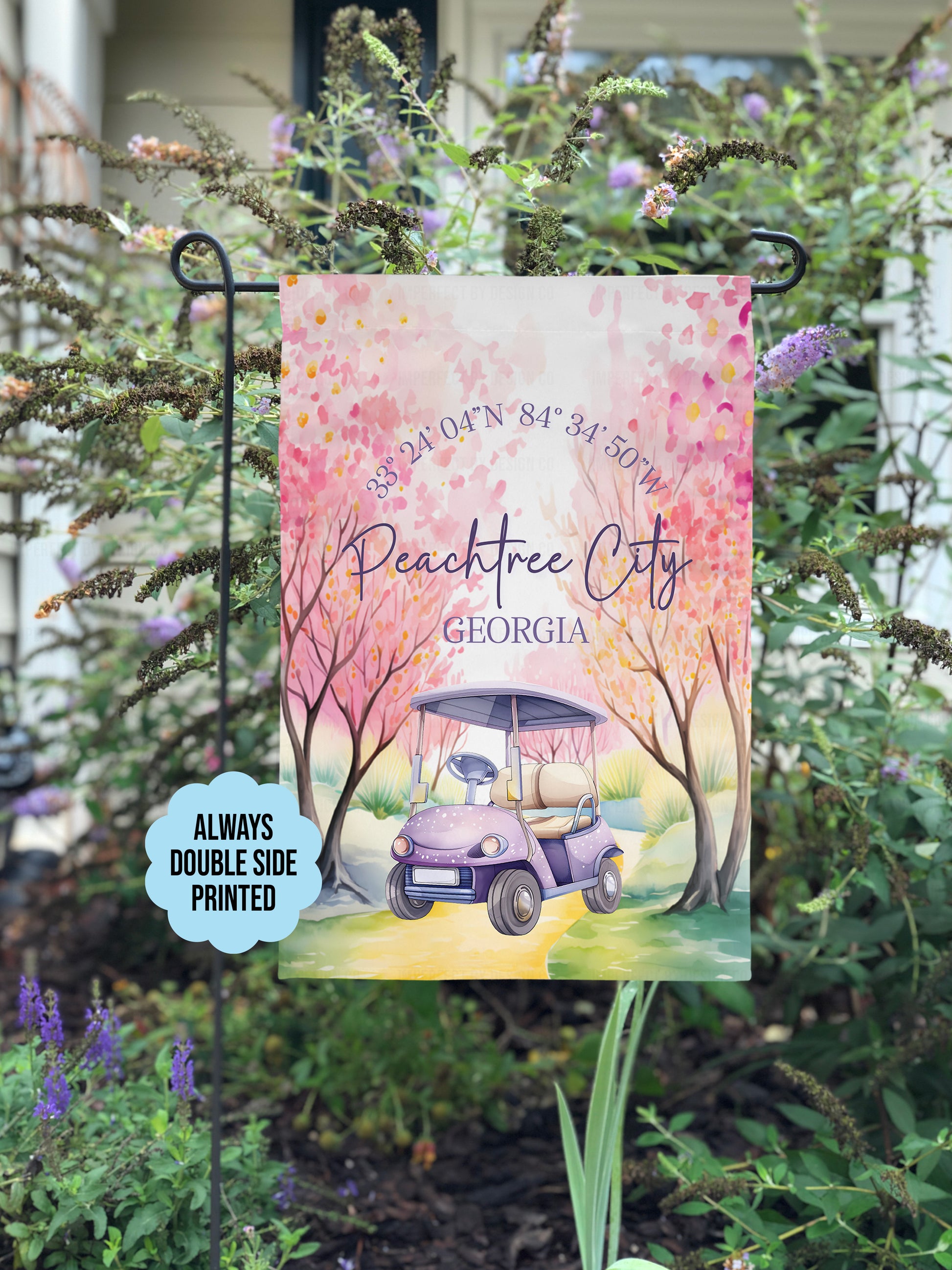 This is an imperfect by design co exclusive design. Garden flag with golf cart and cherry blossoms in Peachtree City, Georgia, on a stand with plants and flowers in the background. Text blurb reads 'always double side printed'