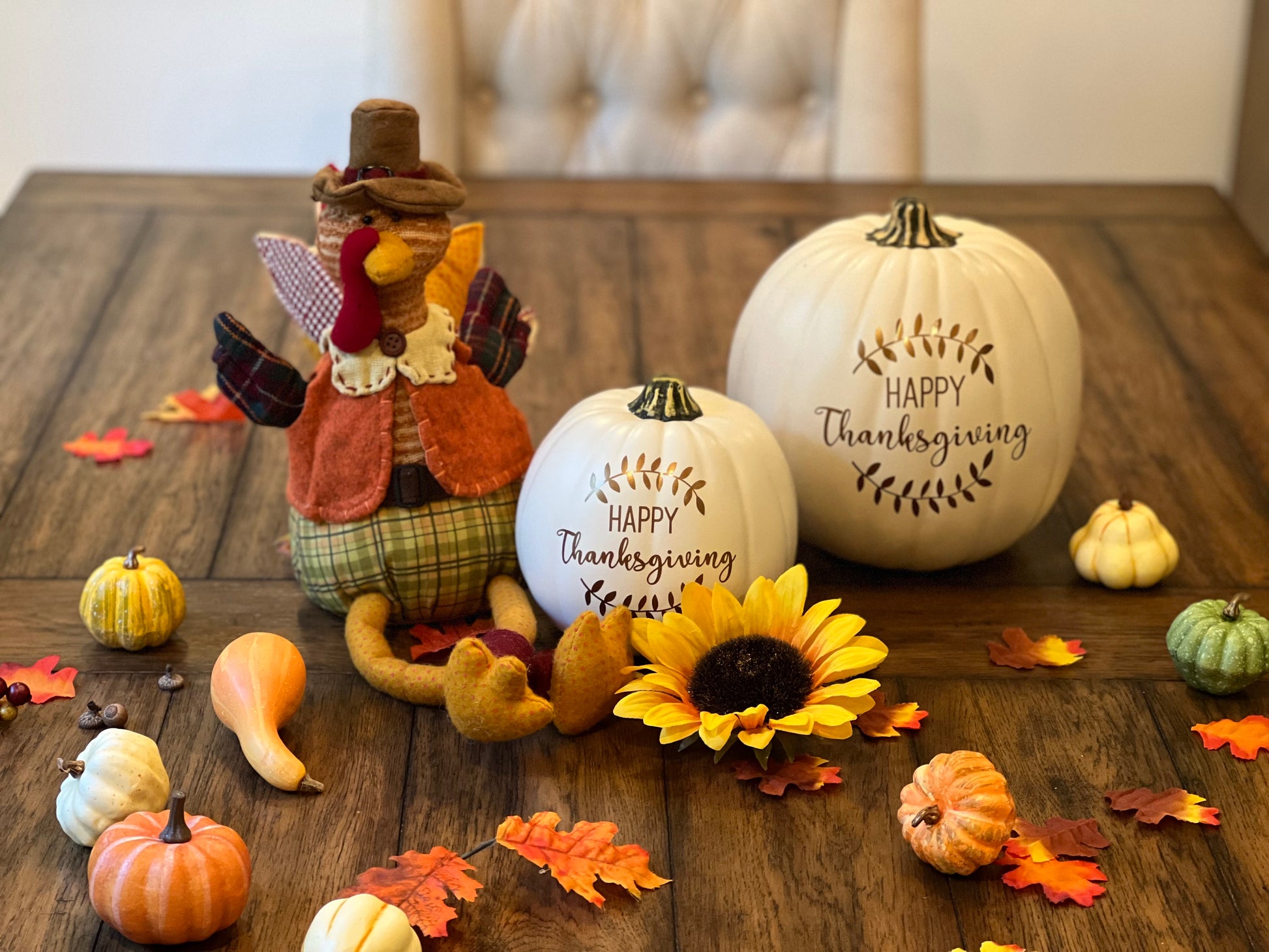 Fall decor pumpkins with Happy Thanksgiving and laurel design sitting on a festively decorated table