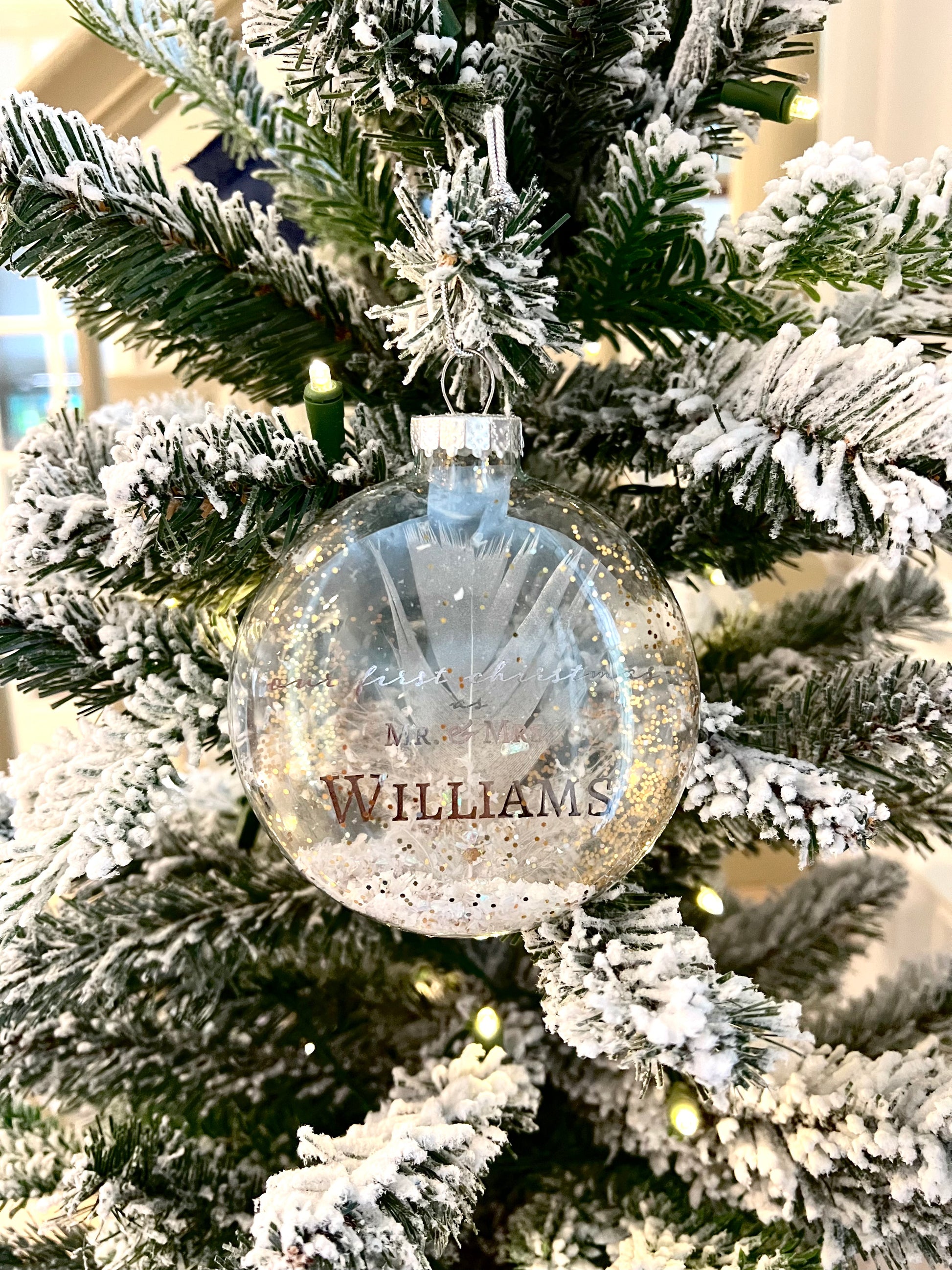 Personalized Wedding Christmas Ornament in Clear Glass – A 4.5 x 4-inch clear glass ornament with the text "Our First Christmas as Mr. & Mrs. [Last Name]" in elegant pewter foil, featuring a silver-tipped white feather and faux snow inside.