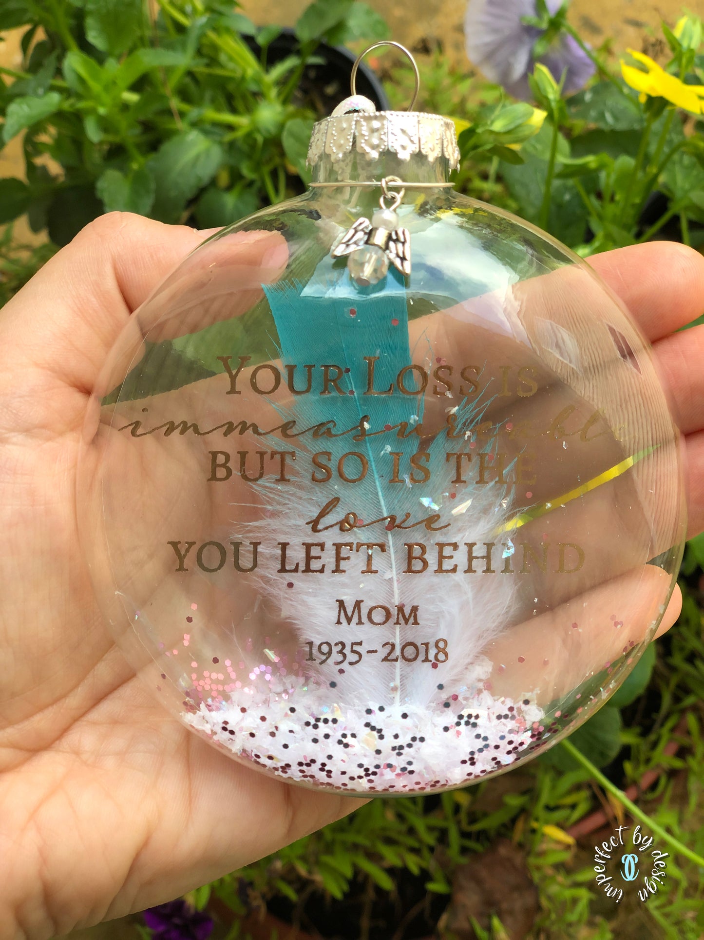 Ornament displaying "Your loss is immeasurable..." text and teal-tipped feather inside.
