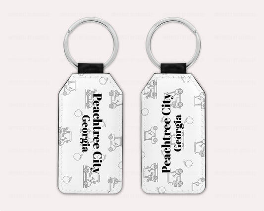 Exclusive design on 2 white faux leather keychain, with a golf cart and peach pattern text reads 'Peachtree City' with 'Georgia' placed right beneath.  View of both sides on a pale pink background | imperfect by design co 