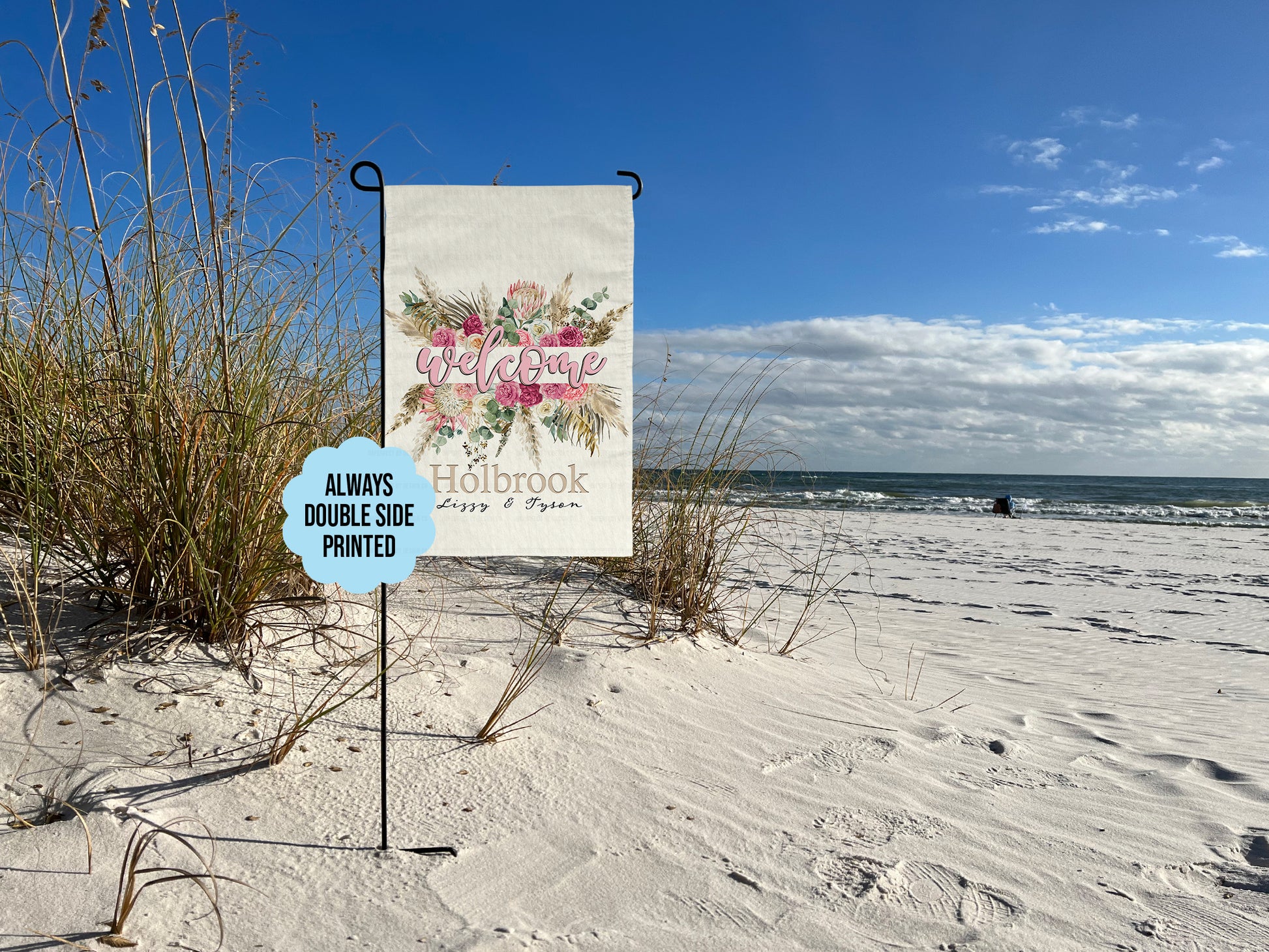 Decorative garden flag with split floral design and personalized text on garden flag stand at beach. Additional text graphic reads 'Always double side printed'