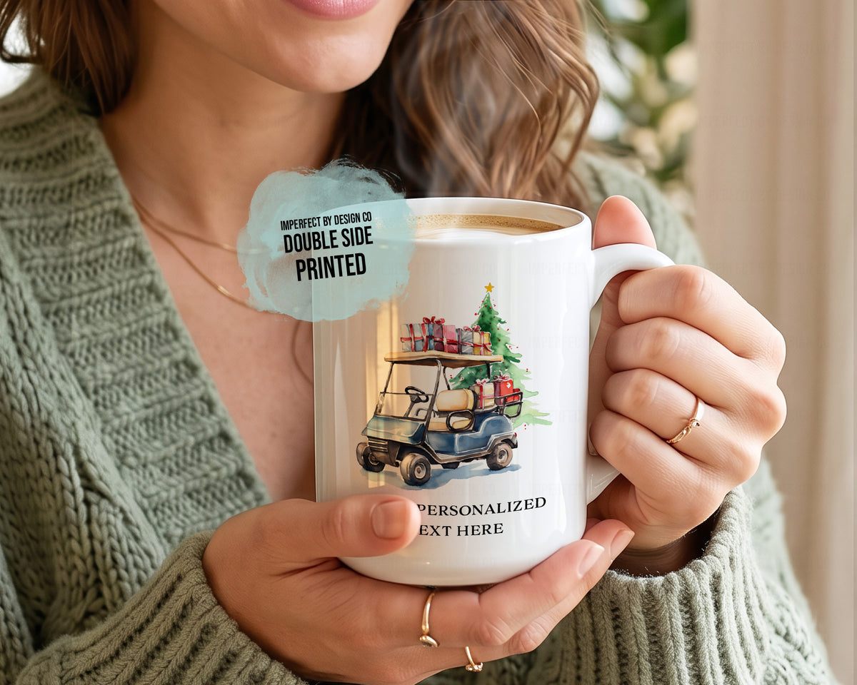 A person in a green knit sweater holds a white ceramic mug with a printed illustration of a golf cart carrying a Christmas tree and gifts. The mug has placeholder text and a light blue circular badge that reads 'IMPERFECT BY DESIGN CO DOUBLE SIDE PRINTED'.