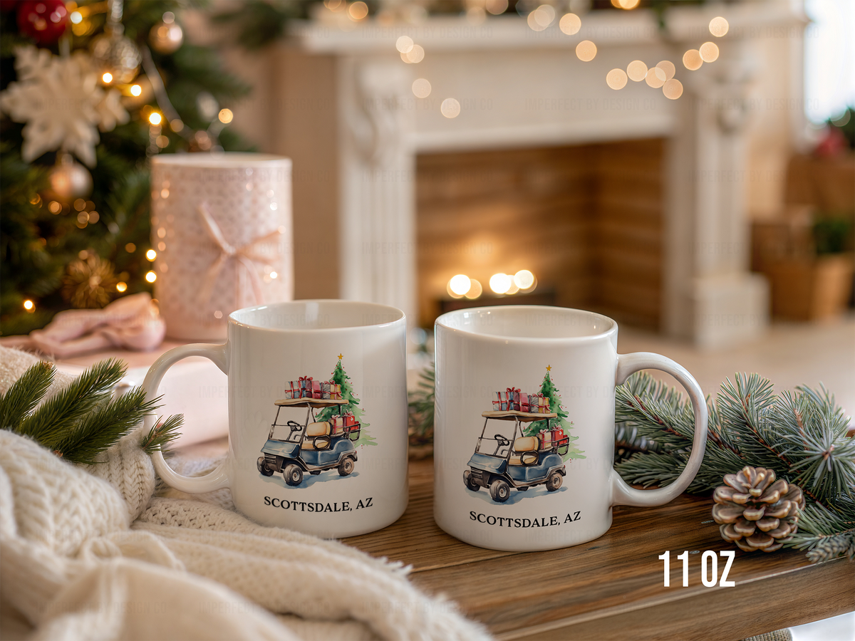 Two white ceramic 11 oz mugs with a golf cart carrying Christmas presents graphic and the text 'OH WHAT FUN' displayed on a wooden table in a cozy holiday setting with a fireplace, tree lights, pine branches, and a knit blanket.
