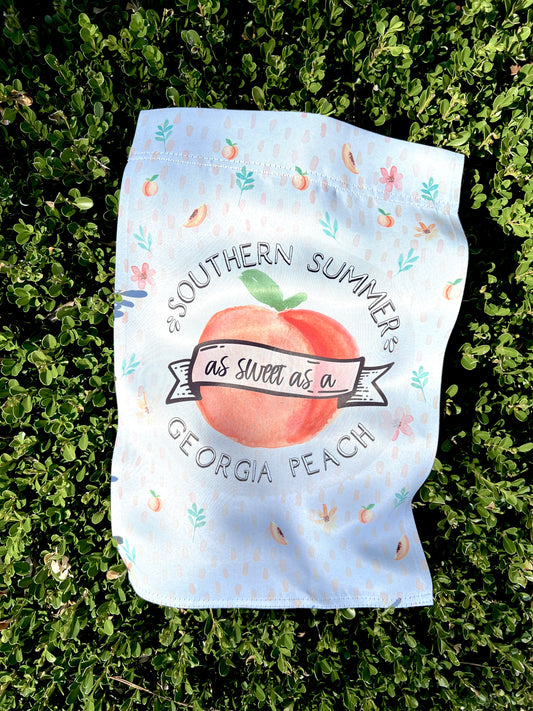 Southern Summer Garden Flag  with a large peach and peach pattern, laid out on a box wood hedge with summer sun shining on it. This flag is not personalized.