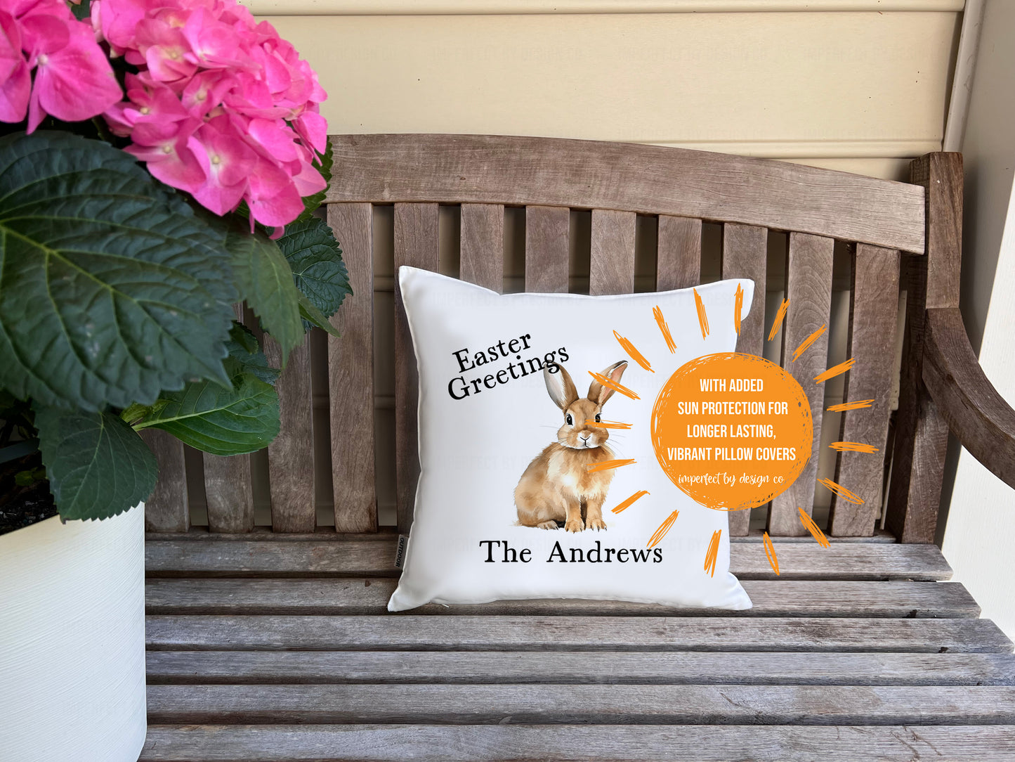 White decorative in-/outdoor pillow advertising pillow cover with Easter design on a wooden bench with flowers.  | imperfect by design co