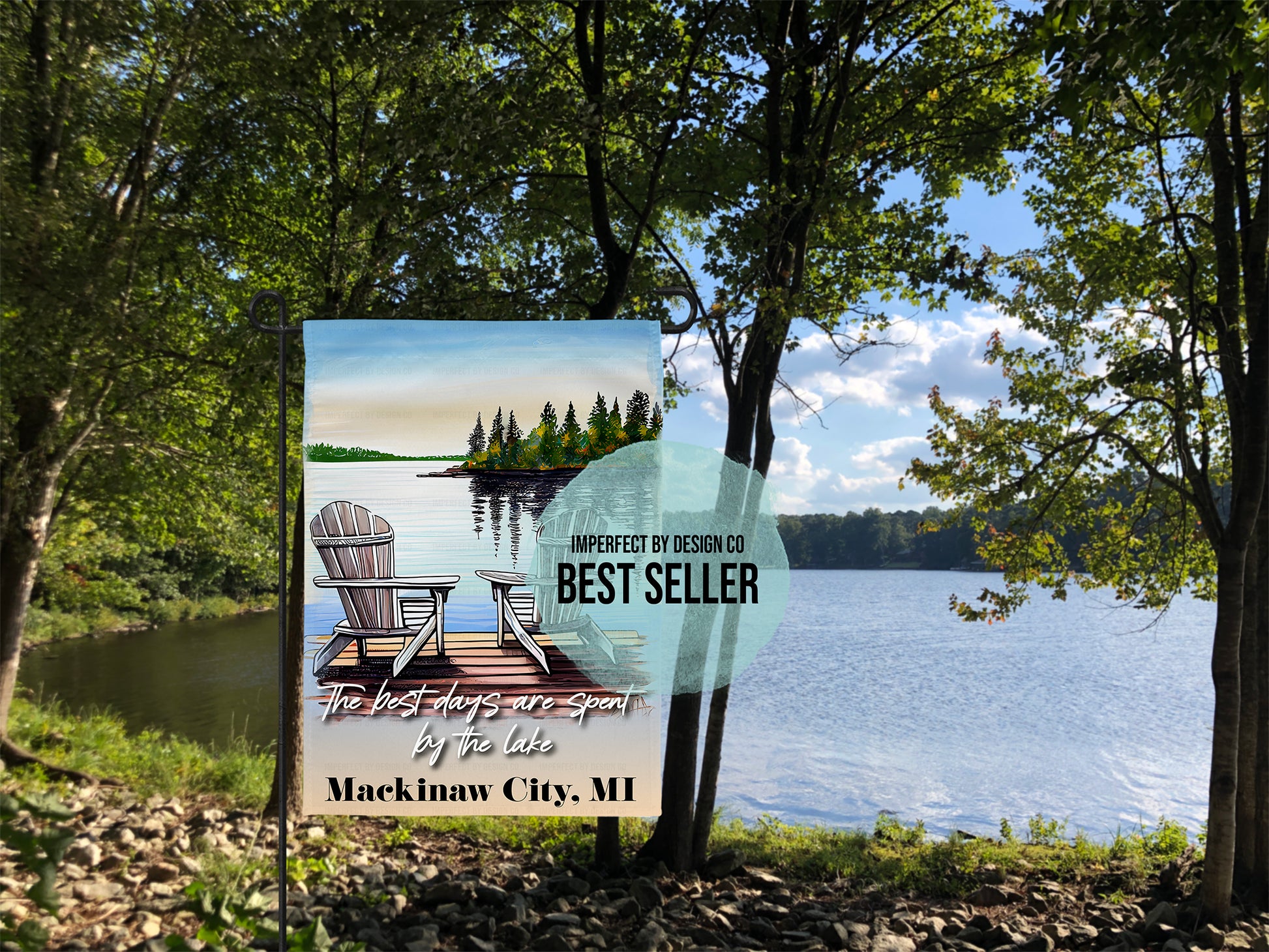 Personalized 'The best days are spent by the lake' garden flag. Placed on garden flag stand in front of scenic lake water front surrounded by trees. Graphic overlay reads 'imperfect by design co best seller'