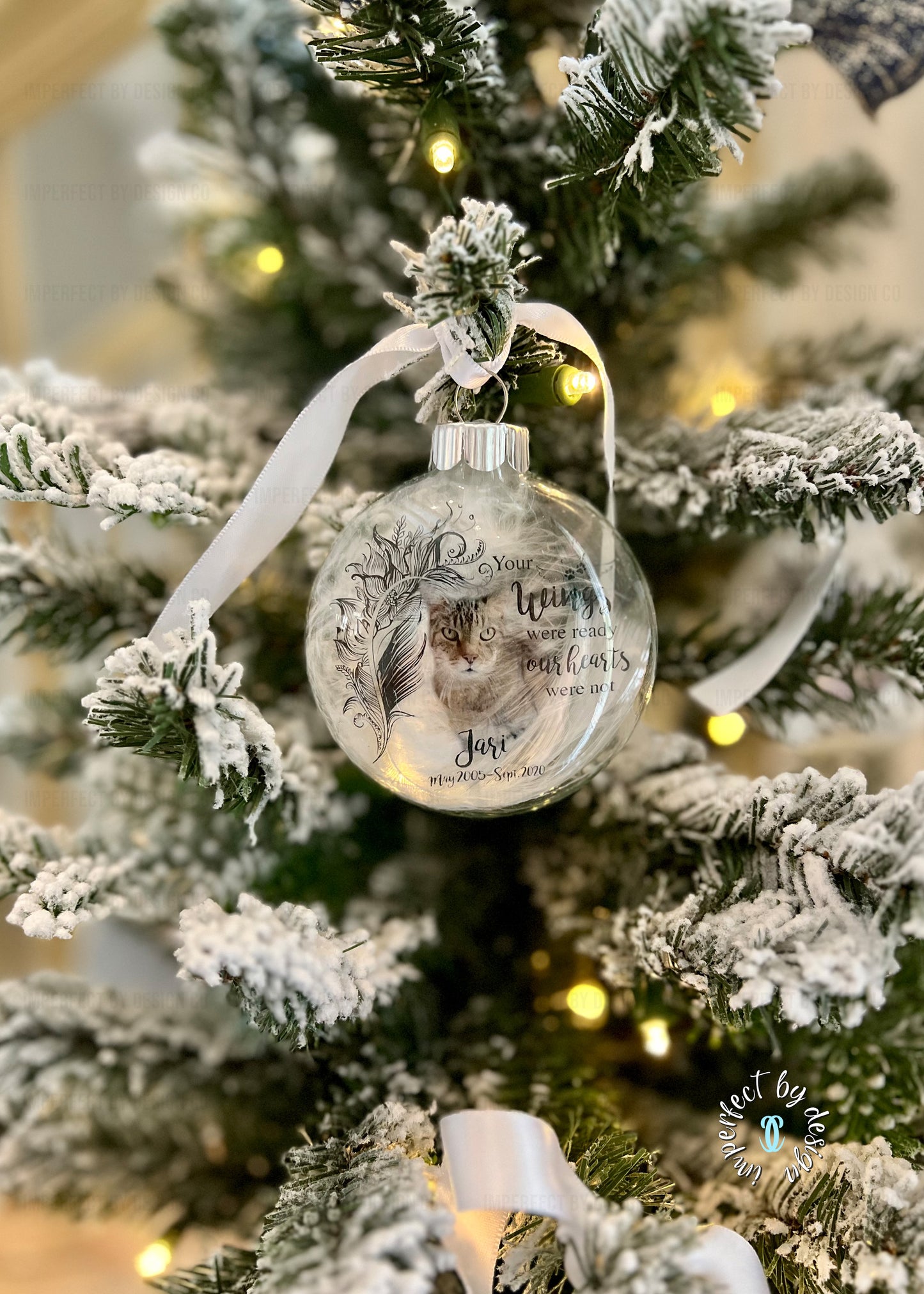 Personalized pet memorial ornament with natural feather, pet's name, years of life, and white ribbon on a flocked Christmas tree.
