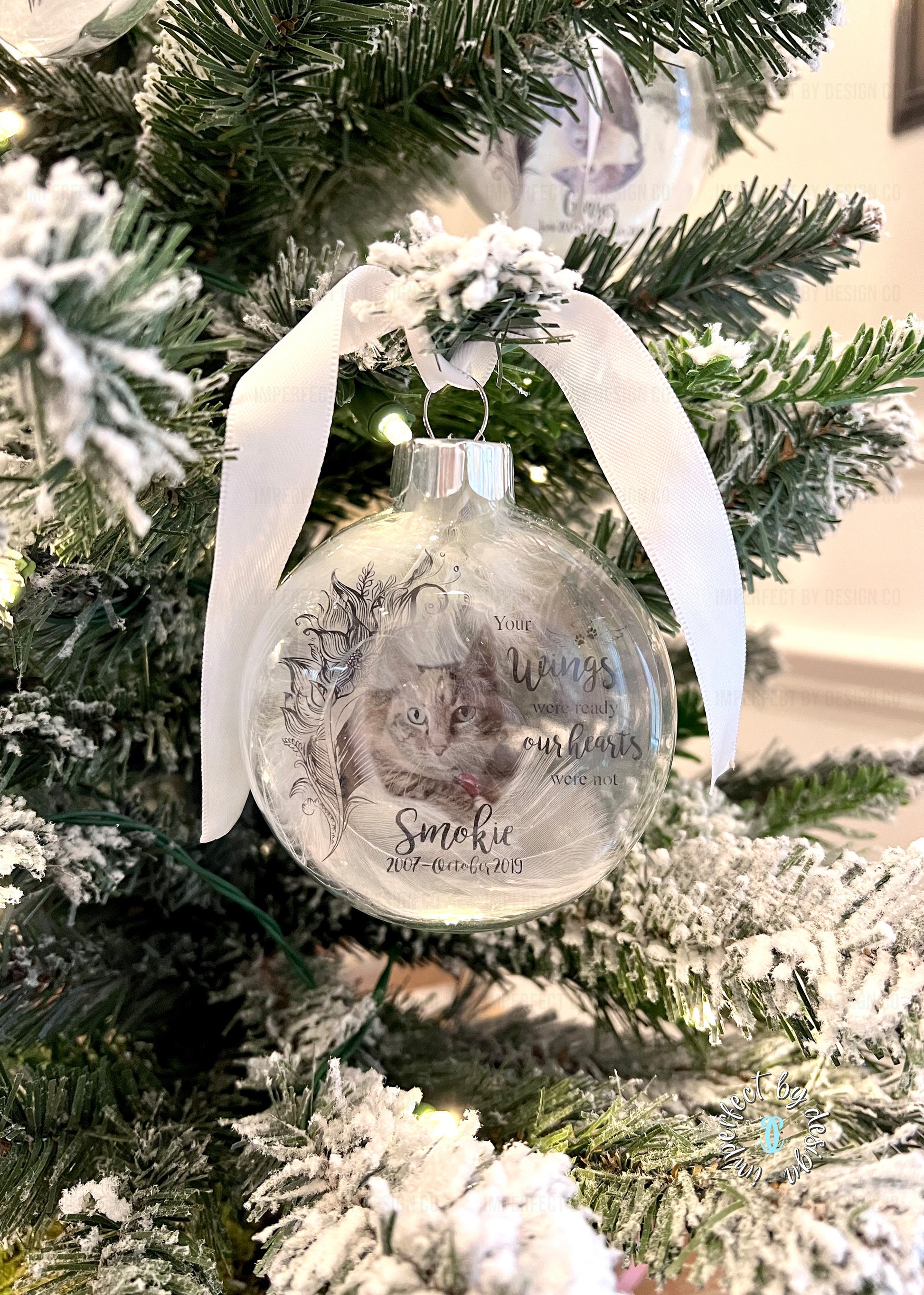 Close-up of glass memorial ornament with silver ribbon, personalized with pet's name, years of life, and memorial quote.
