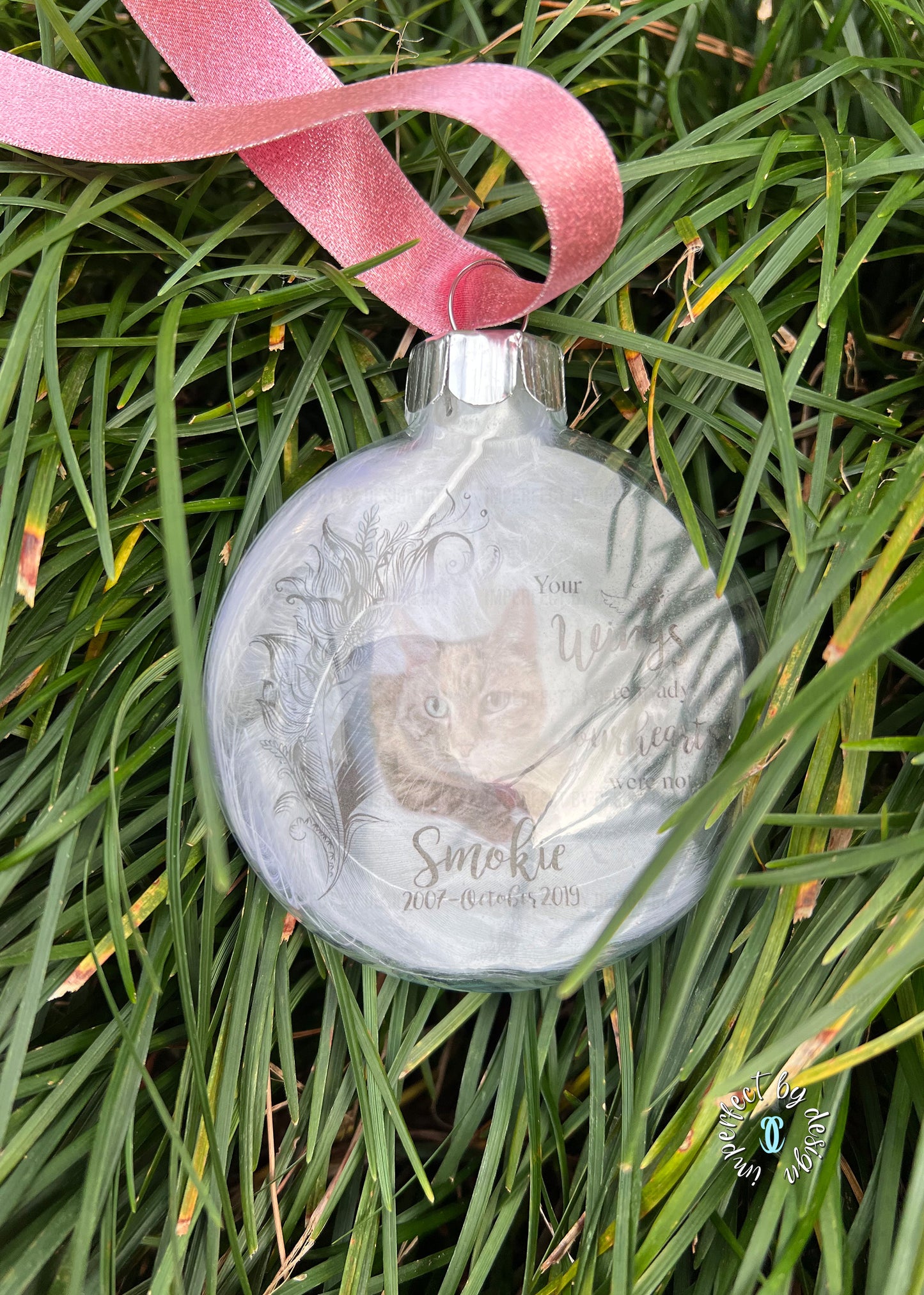 Pet memorial ornament with pink ribbon and custom pet name, years of life, and natural feather inside.
