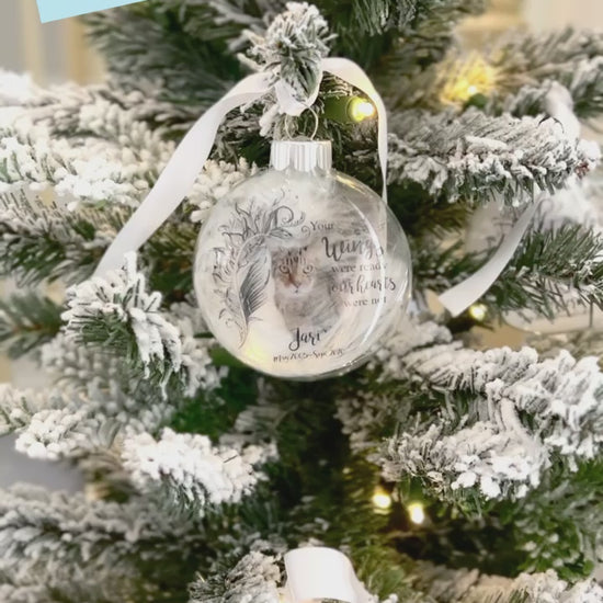 Video of Pet memorial ornament with white ribbon and custom pet name, years of life, and natural feather inside.
