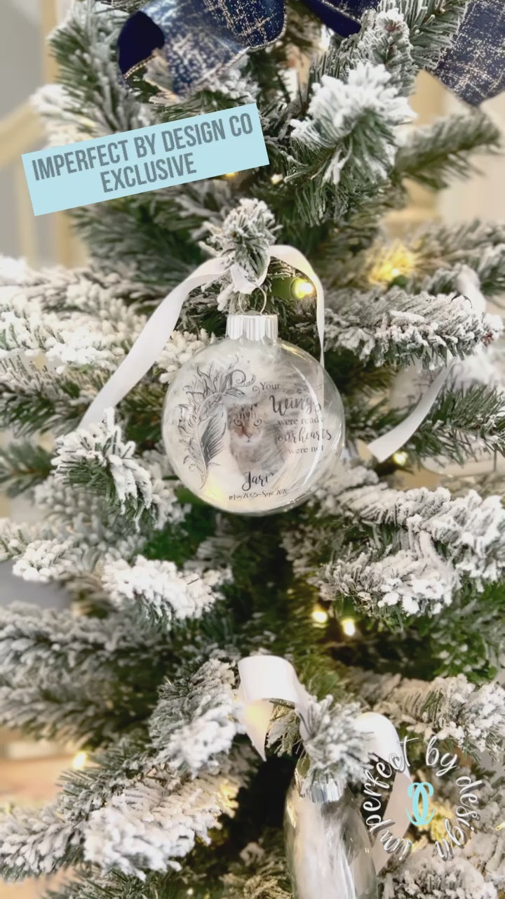 Video of Pet memorial ornament with white ribbon and custom pet name, years of life, and natural feather inside.
